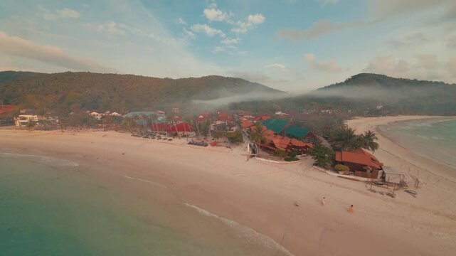 Fast cinematic FPV drone footage cruising low over the sandy coastal beach and ocean waves of Redang Island during a beautiful golden sunrise