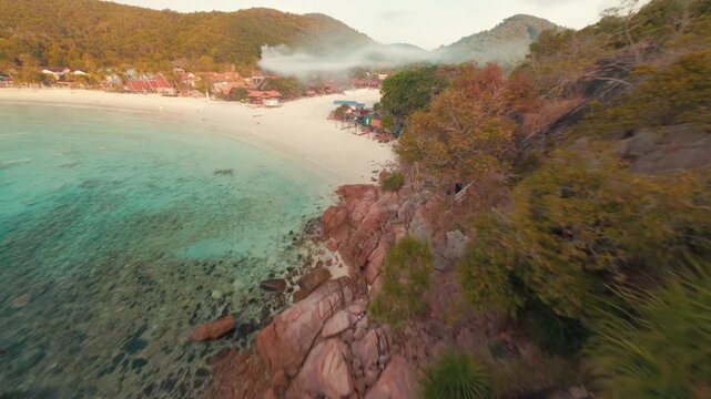 Fast cinematic FPV drone footage cruising low over the sandy coastal beach and ocean waves of Redang Island during a beautiful golden sunrise