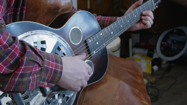 Guitar tech in leather apron plays National Steel guitar in work shop