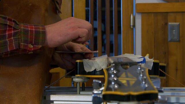 Closeup detail: Guitar tech in shop fills chips in electric guitar neck