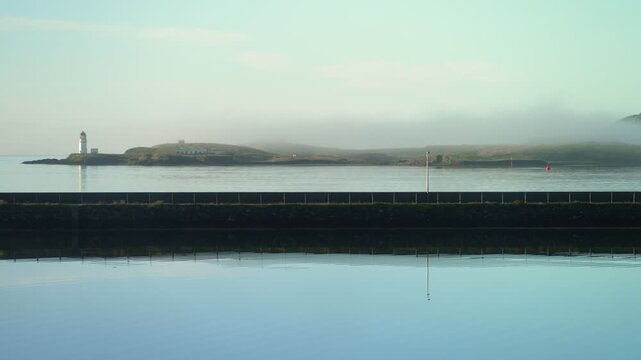 Static shot of morning mist rolling over Stornoway lighthouse in summer.