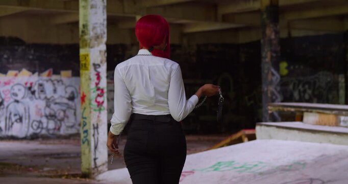 A girl with fiery red hair wears her white shirt and black slacks to a local skate park, posing in front of a giant, mural-covered quarter pipe.
