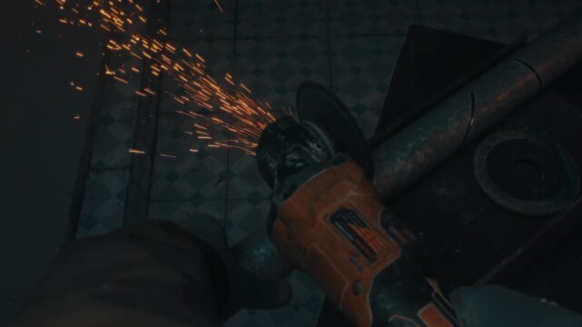 Angle grinder cutting metal pipe producing shower of sparks, worker pov top down angle