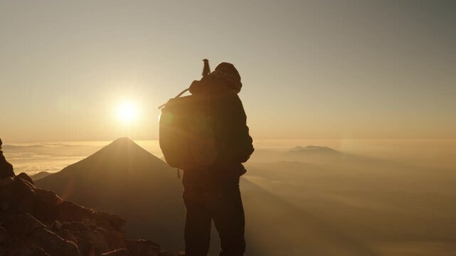 Hiker standing with arms open at sunrise above clouds