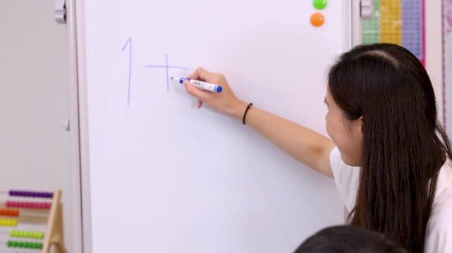 Female Teacher Writing Simple Math Equation on Classroom Whiteboard