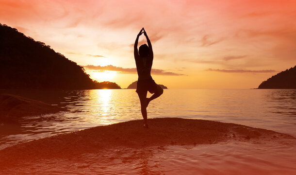 silhouette of woman practicing yoga tree pose on the beach at sunset