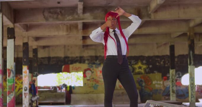 An office-clad girl with red hair walks across the smooth concrete of a skate park surrounded by walls of expressive, high-contrast street art.