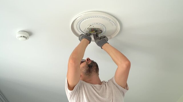 Electrician installs ceiling LED lamp on suspended ceiling. Hands connect wires of lamp frame. Installation light