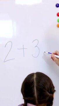 Teacher Writing Math Equation on Whiteboard for Young Student in Classroom