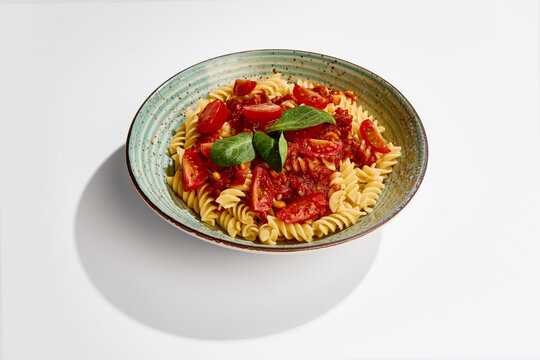 Fusilli pasta with tomato sauce, cherry tomatoes and basil served on ceramic plate on white background side view. Concept of italian cuisine, restaurant menu, food styling and healthy eating.