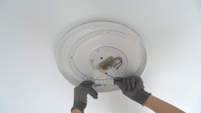 Close up of electricians hands installs ceiling LED lamp on suspended ceiling. Hands connect wires of lamp frame. Current check. Installation light