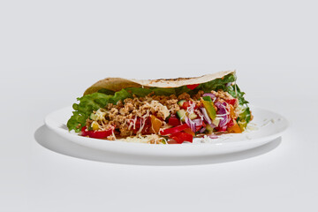 Fototapeta premium Side view tortilla wrap filled with vegetables, minced meat and cheese on white plate on clean background. Concept of fast dining, takeaway culture, delivery service and food choice in busy lifestyle.