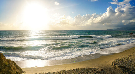 Sunny beach with waves and cloudy sky on a summer day
