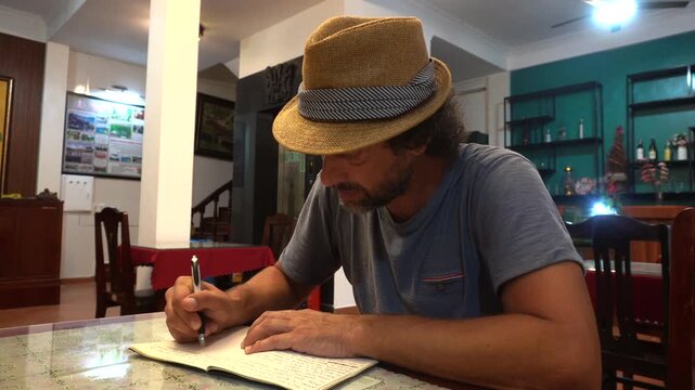 A 40-year-old male traveler writes a travel diary during a hotel stopover - write a travel report to remember the stages and experiences you had on your trip