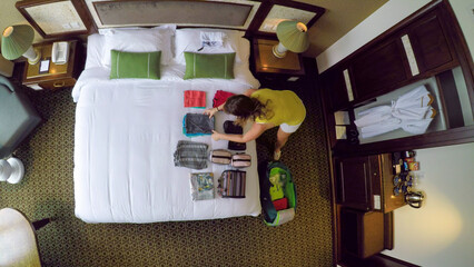 Fototapeta premium TOP DOWN: Female traveler opens her travel bag and unpacks her clothes onto bed