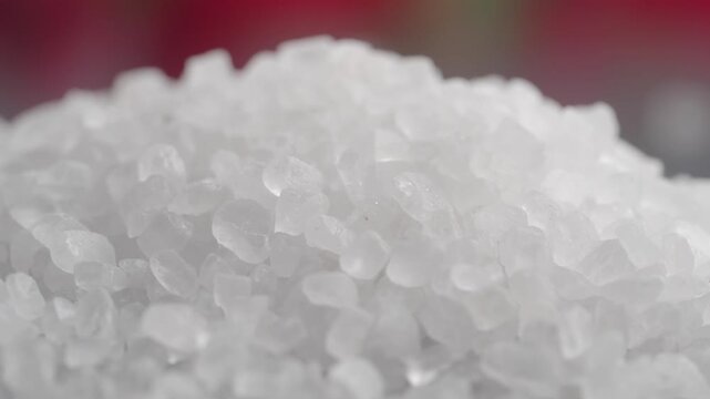 Close up slow motion shot of white sea salt grains forming a small sparkling hill in soft studio lighting
