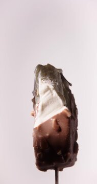 Closeup Video of bitten off Chocolate Almonds Ice Cream Stick Bar Rotating on White Background. Vertical Studio Shot, Local Light, 60 fps.