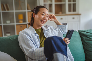 Asian woman relaxing on sofa using smart phone at home