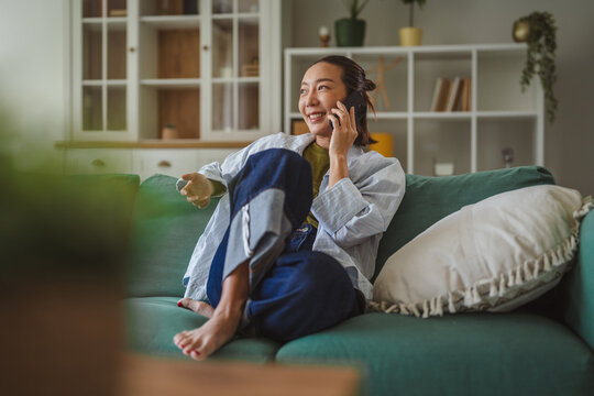 Asian woman talking on smart phone smiling happily at home