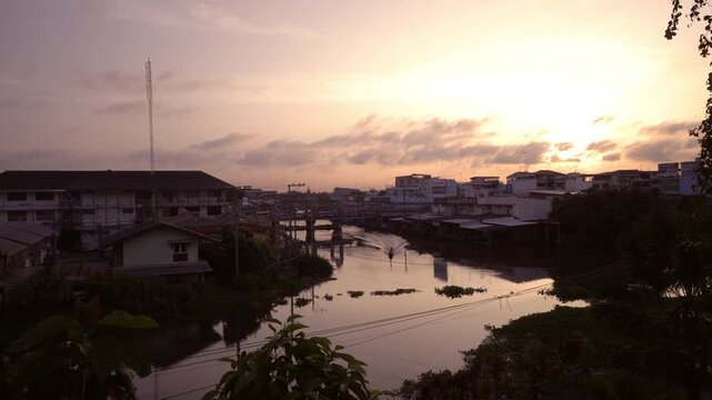 Morning time-lapse of a boat driving on the river with city buildings and beautiful sunrise sky in Samut Prakan Thailand