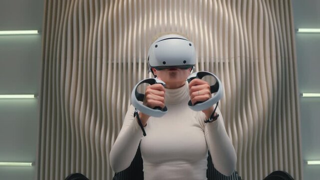 Caucasian cyberpunk woman in VR glasses moving hands in air hologram playing virtual reality holding controller play video game female girl in futuristic white room sitting in chair futurism metaverse