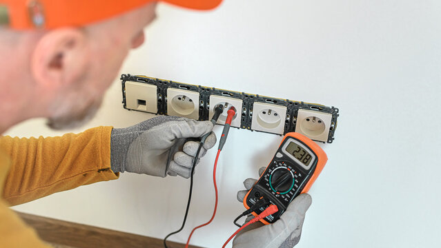 Electrical installation. The electrician's hands measure the voltage in an electrical outlet using a multimeter during installation a wall multi pack socket.