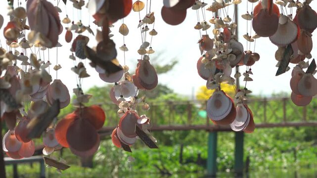 Sea shell mobile hanging and swaying in the gentle breeze with sunlight on green bokeh background in 4K seamless loop_02