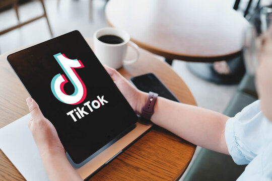 Bangkok, Thailand. March 19, 2026; Over the shoulder view of a person using a tablet to access the TikTok social media application while relaxing at a wooden cafe table.