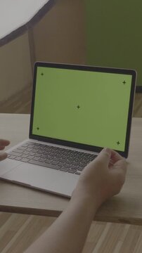 Vertical 9:16 Over the shoulder mid shot of businessman hands typing on green screen laptop display with tracking markers. V-Log footage on modern laptop mockup on wooden desk. Ideal for tech demo or 
