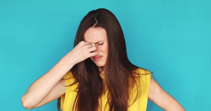 Upset young woman touching her bridge of nose and forehead feeling tired or having headache isolated on blue background, exhausted female brunette expressing regret, disappointment or facepalm gesture