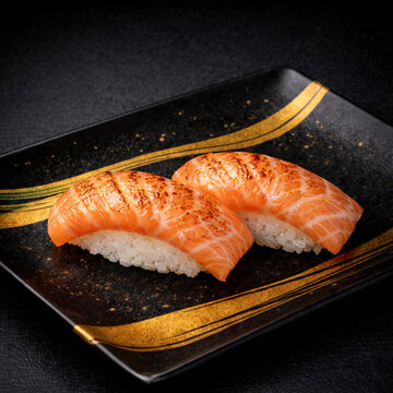 Premium fresh seared salmon aburi sushi on a luxury black ceramic plate with gold brushstrokes, dramatic lighting, high-end traditional Japanese cuisine.