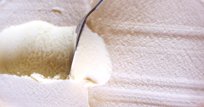 Close up of a metal spoon scooping smooth creamy vanilla ice cream or frozen yogurt, delicious white dairy dessert texture with soft ridges and frosty surface, organic sweet summer treat top view