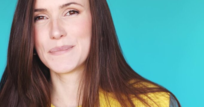 Close-up video of a beautiful young woman enjoying a delicious snack, licking a spoon with pleasure and smiling shyly at the camera, isolated on a bright turquoise background.