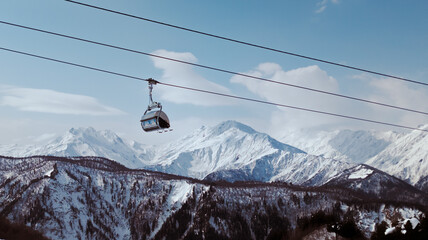 Ski lift gondola moving down against majestic snowy mountain range. © Vadzim