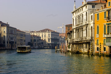 A water taxi navigates the Grand Canal in Venice, Italy, passing by historic buildings and gondola mooring poles. © Nick