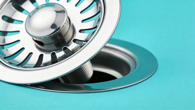 Close-up of a shiny silver stainless steel kitchen sink drain and strainer basket on a vibrant turquoise background, highlighting plumbing hardware and home improvement concepts