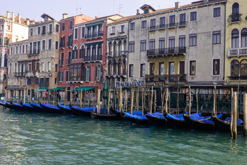 Obraz premium A row of gondolas are moored along a canal in Venice, Italy, with historic buildings lining the waterfront.