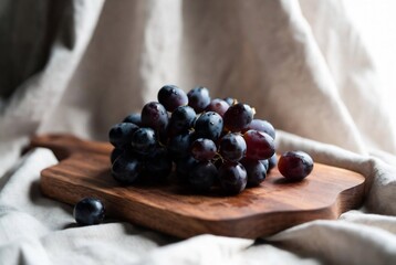 Naklejka premium A cluster of dark grapes rests on a wooden board, draped with fabric.
