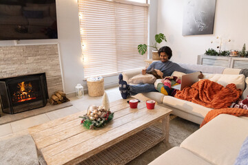 Fototapeta premium Couple sitting on right side of sectional sofa using laptop under orange blanket by fireplace