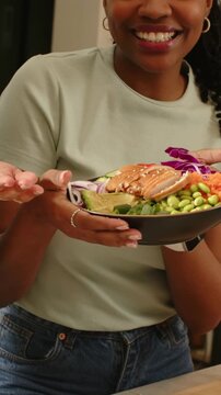 Vertical video: Recording woman in green tee holding salmon bowl for camera at counter aid helping