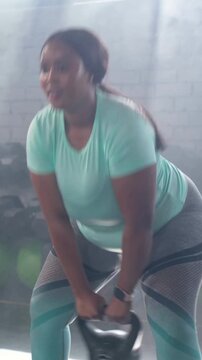 Vertical video: Bending woman in mint top gripping 5 KG kettlebell, swinging for strength in gym