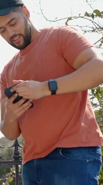 Vertical video: Reaching man in orange tee retrieving phone from hip at overlook to check screen