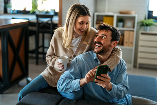 Happy couple relaxing at home with coffee, enjoying online shopping and shared digital experiences