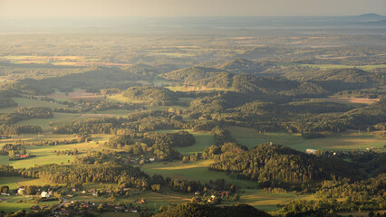 Fototapeta premium Scenic aerial panorama of the Czech countryside with green fields, forests and small villages seen from Jested mountain during warm evening sunset light.