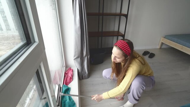 Kneeling Lady Washes Lower Glass. Kneeling Woman Performs Domestic Cleaning With Satisfying Results