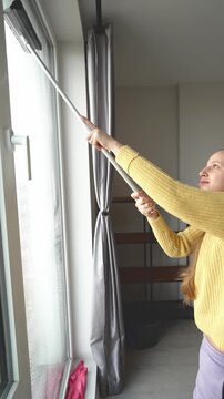 Woman Cleans Window. Calm Domestic Scene Showing Woman Meticulously Cleaning Window In Cozy Apartment