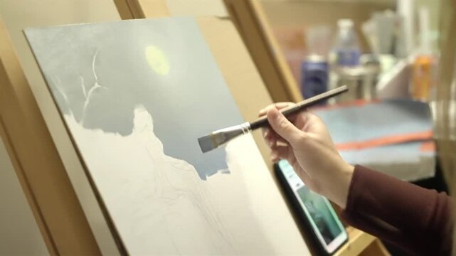 Artist hand painting on canvas with brush in studio close up shot