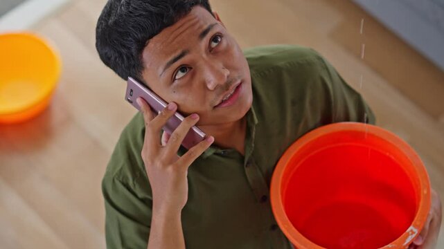 Asian homeowner using smartphone to report home water damage from leaky roof