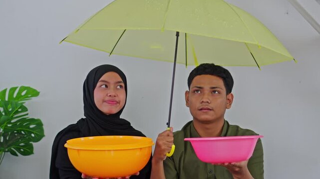 Asian couple catching water from leaky roof using basins and umbrella