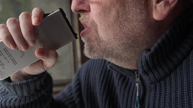 A man speaks with emotional intensity into a vintage analogue voice recorder. Cinematic profile shot for vintage communication and true crime narratives.